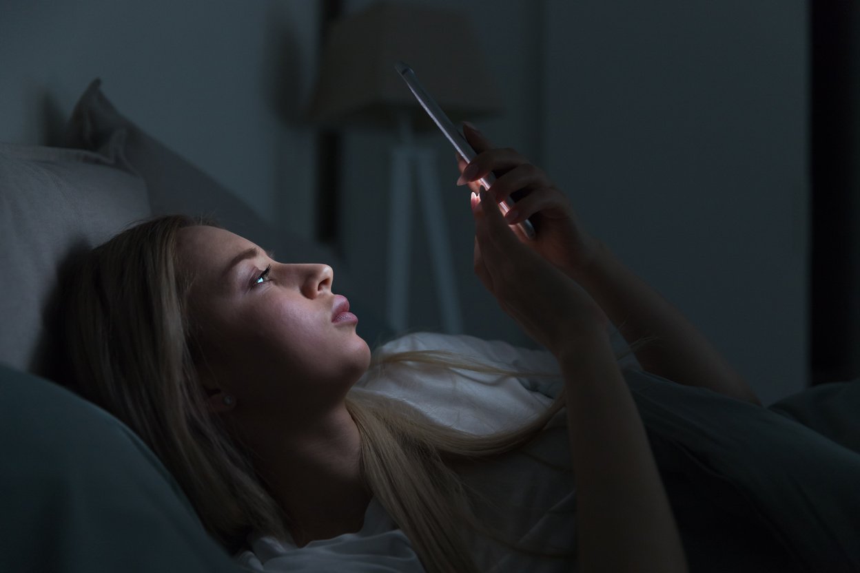 Exhausted Woman Lying in Bed Using Mobile Phone