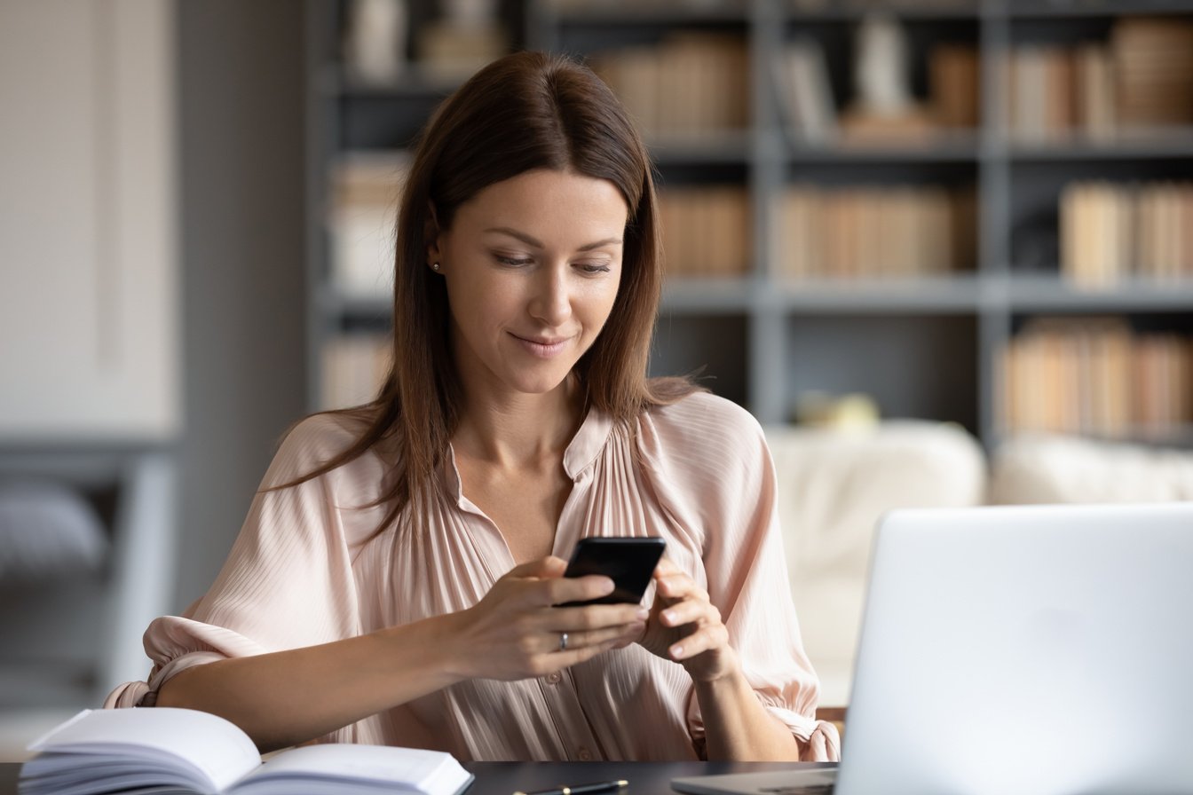 Happy woman looking at phone screen, distracted from work