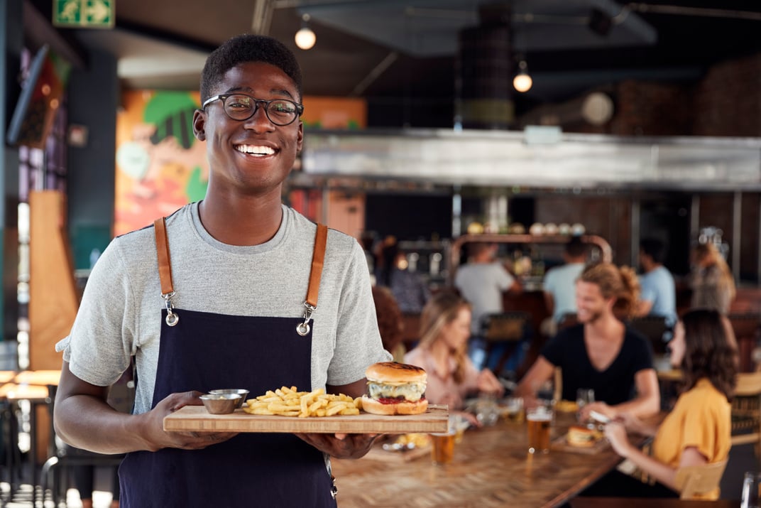 Portrait of Waiter Serving Food to Customers in Busy Bar Restaur